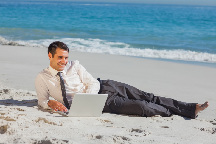 Young businessman lying on the sand using his laptop